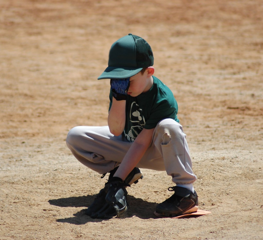 Little boy baseball player covering his face with his hand.