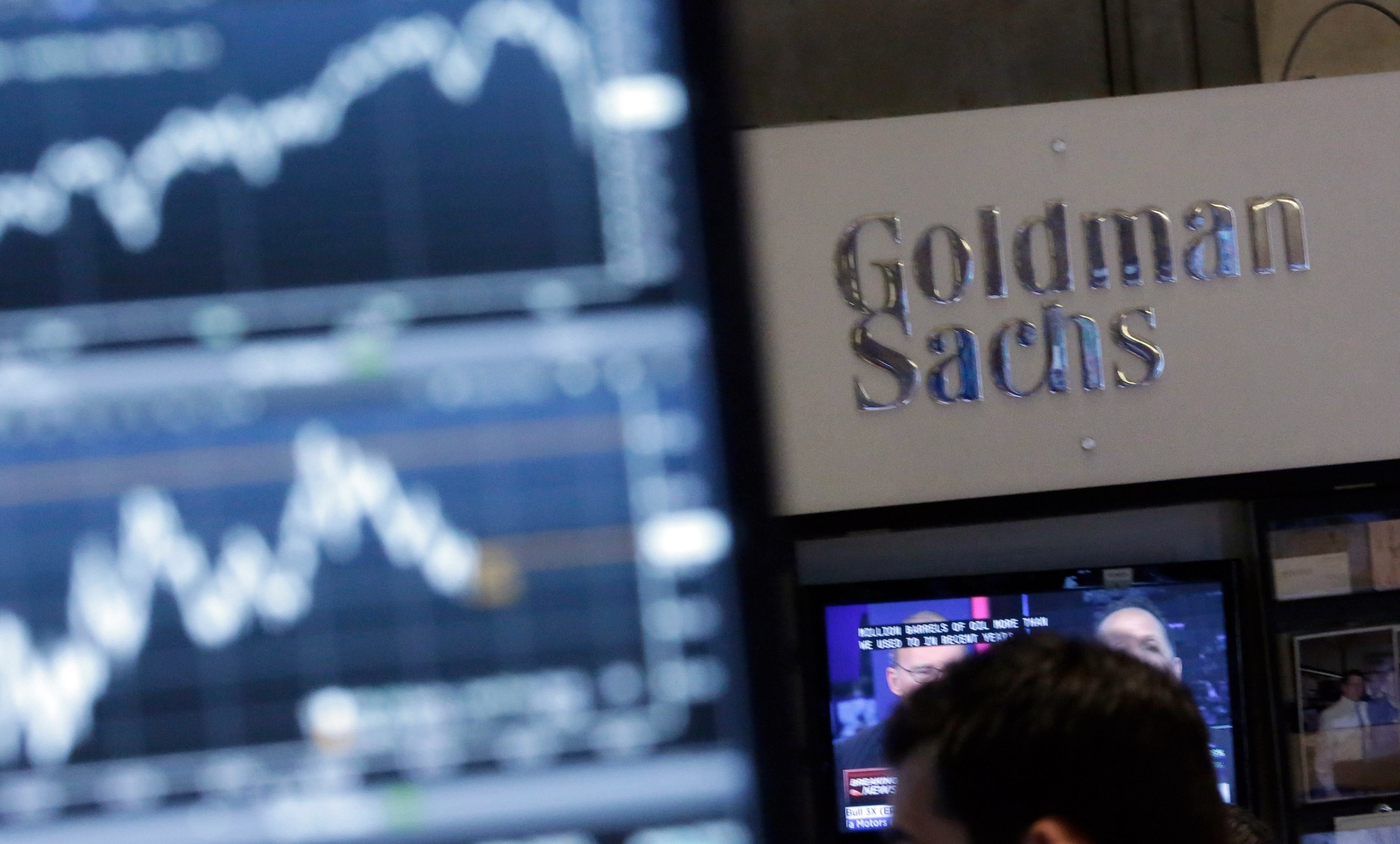 An image of a screen at a trading post on the floor of the New York Stock Exchange is juxtaposed with the Goldman Sachs booth
