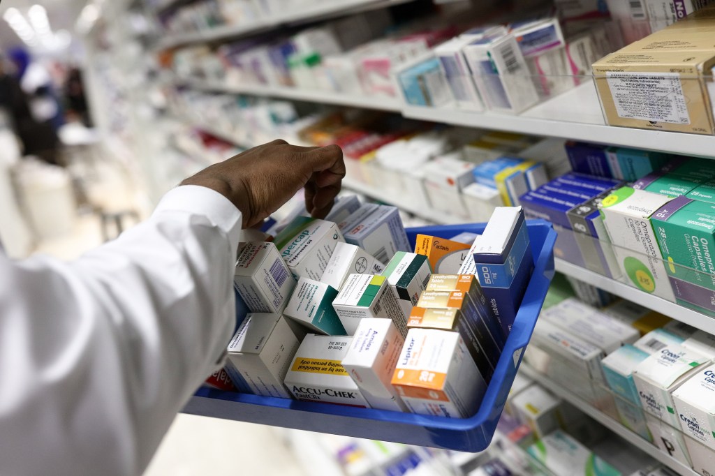 A pharmacist collects packets of boxed medication from the shelves of a pharmacy.