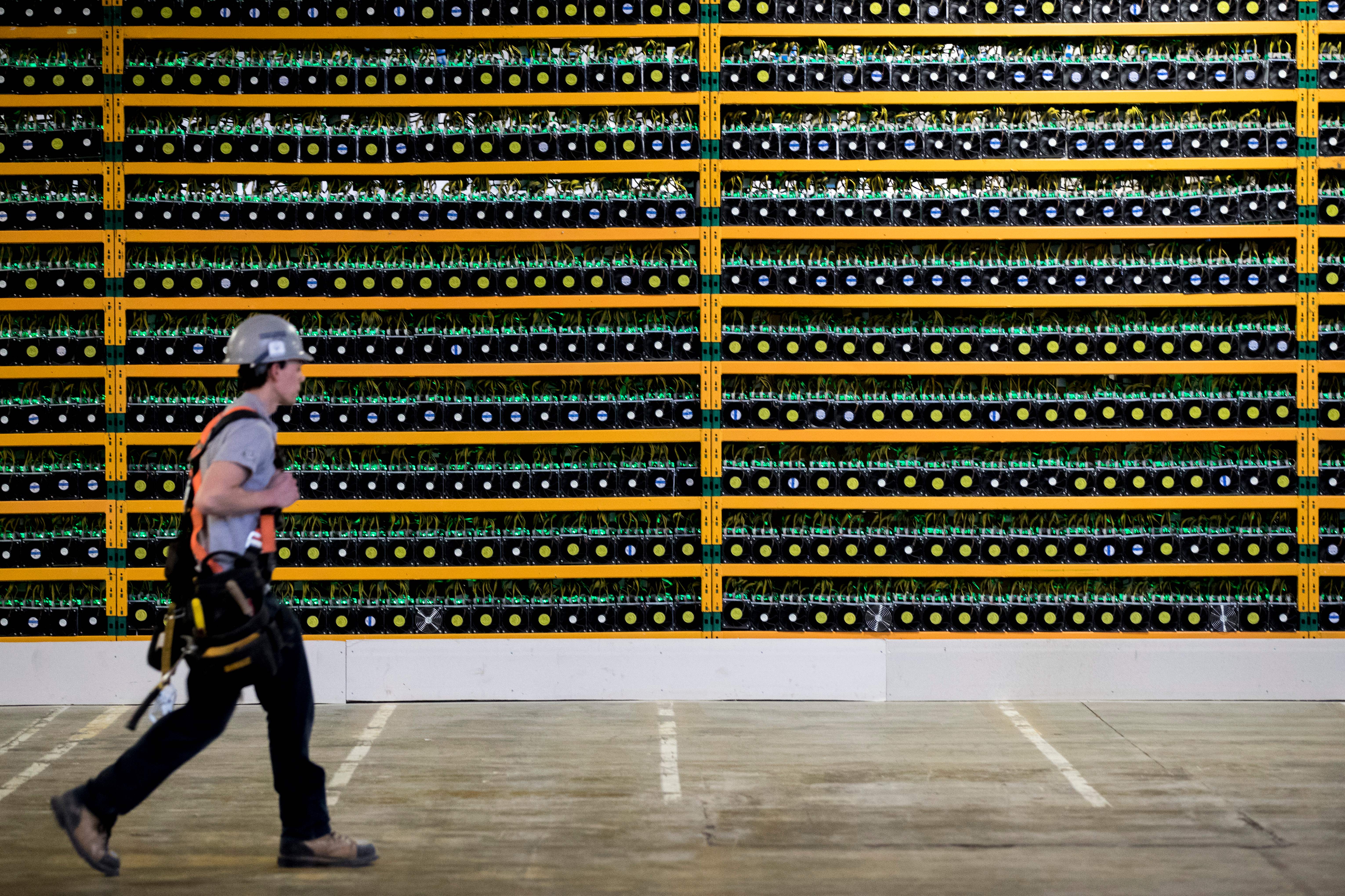 Image of a person walking past a wall of bitcoin mining rigs