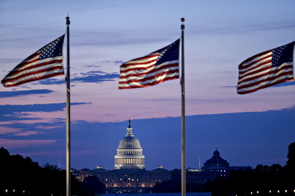 The U.S. Capitol building stands past American flags before sunrise in Washington