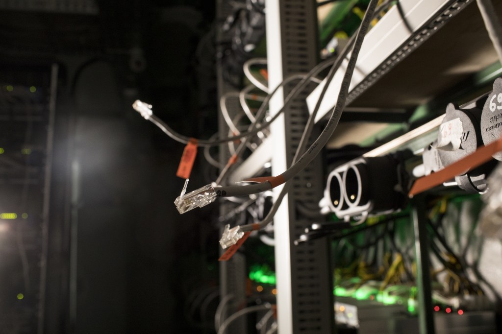 Disconnected ethernet cables hang from shelves containing cryptocurrency mining rigs in a cargo container