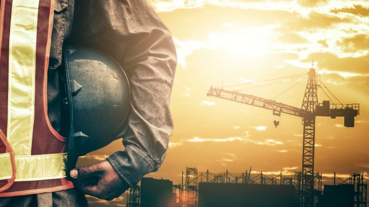 Midsection Of Manual Worker Holding Hardhat Against Sky During Sunset