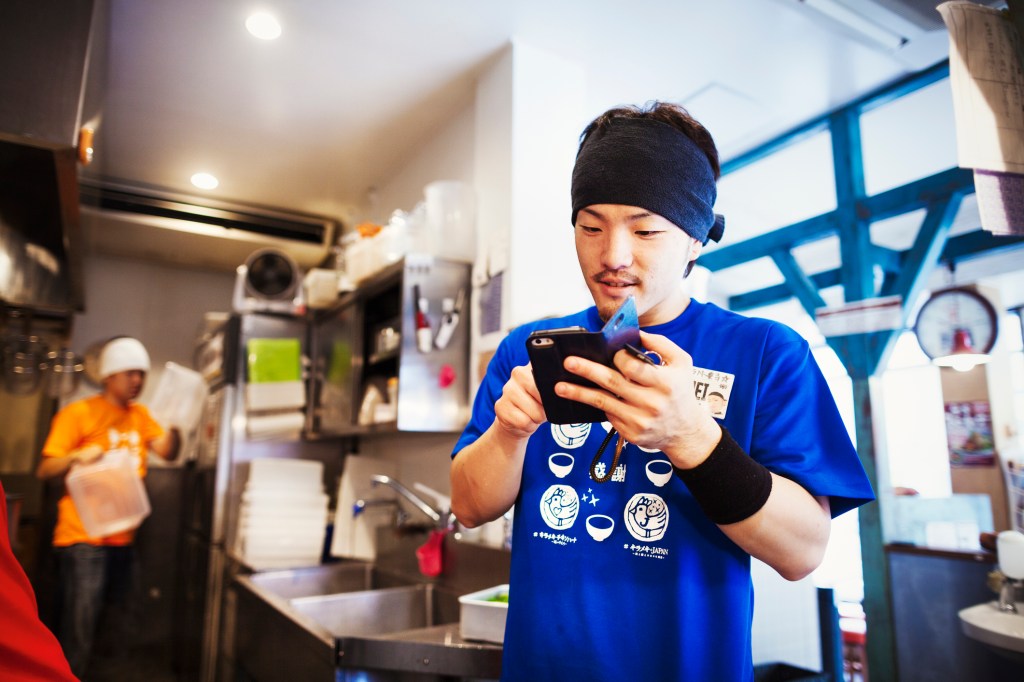 Ramen noodle shop, staff preparing food. A chef using a smart phone in a kitchen.