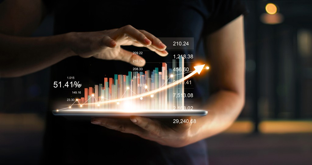 Businessman holding tablet and showing a growing virtual hologram of statistics, graph and chart with arrow up on dark background. Stock market. Business growth, planning and strategy concept.