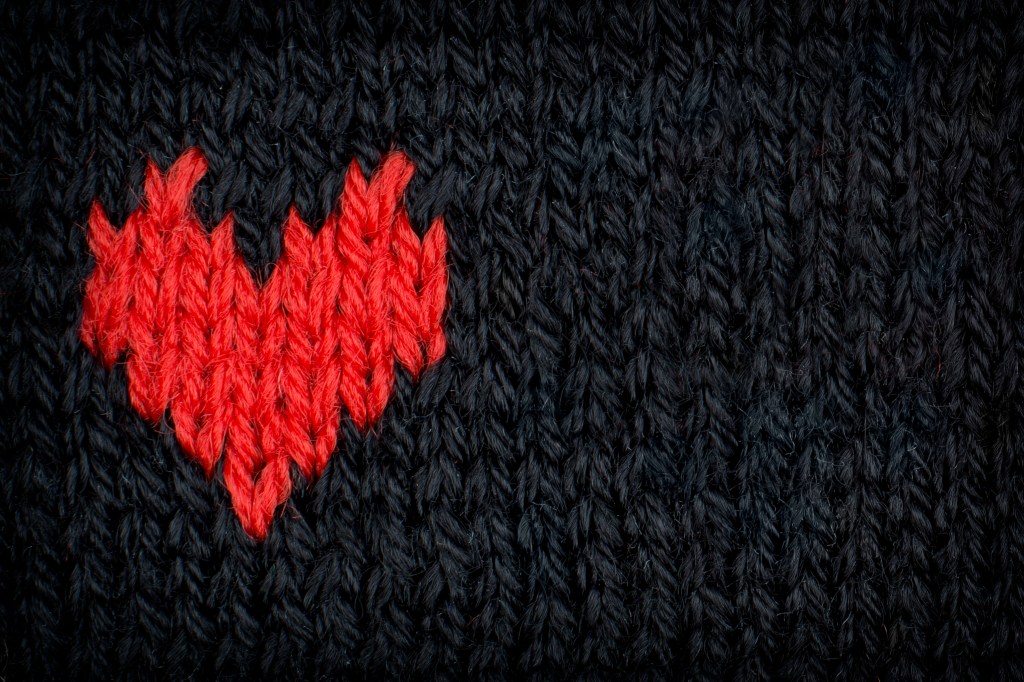 Knitted red heart made of yarn on a black background.