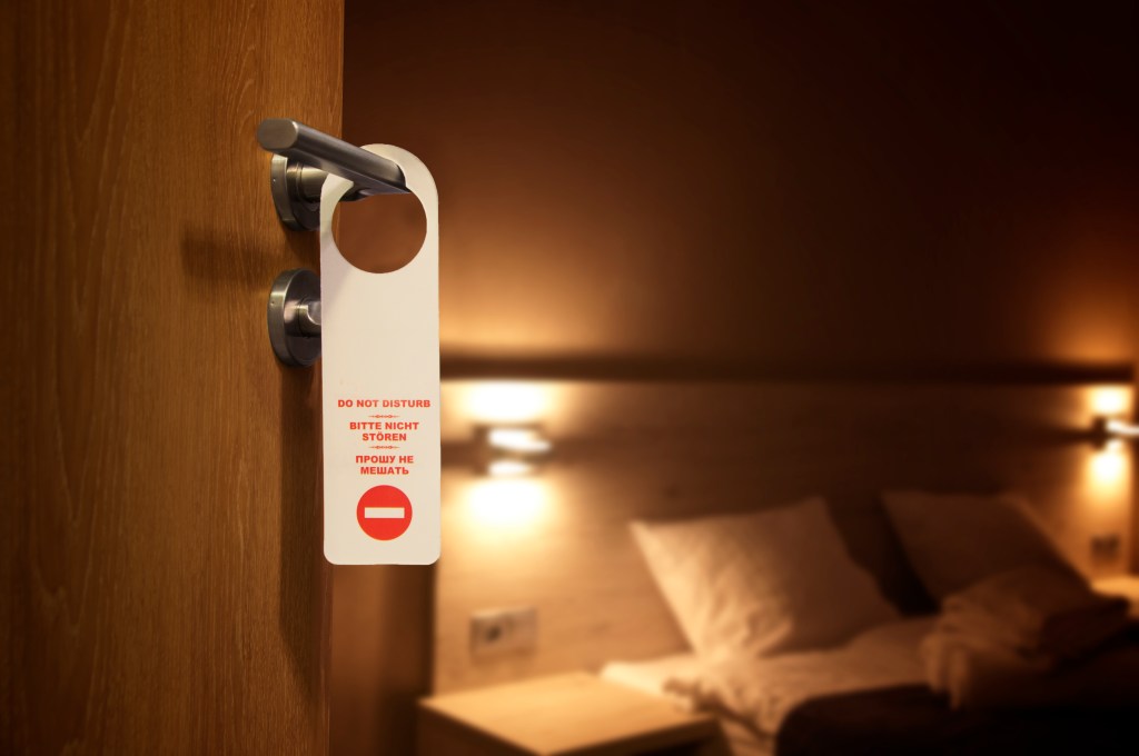Do not disturb sign on the handle of open hotel room door with bed in the background
