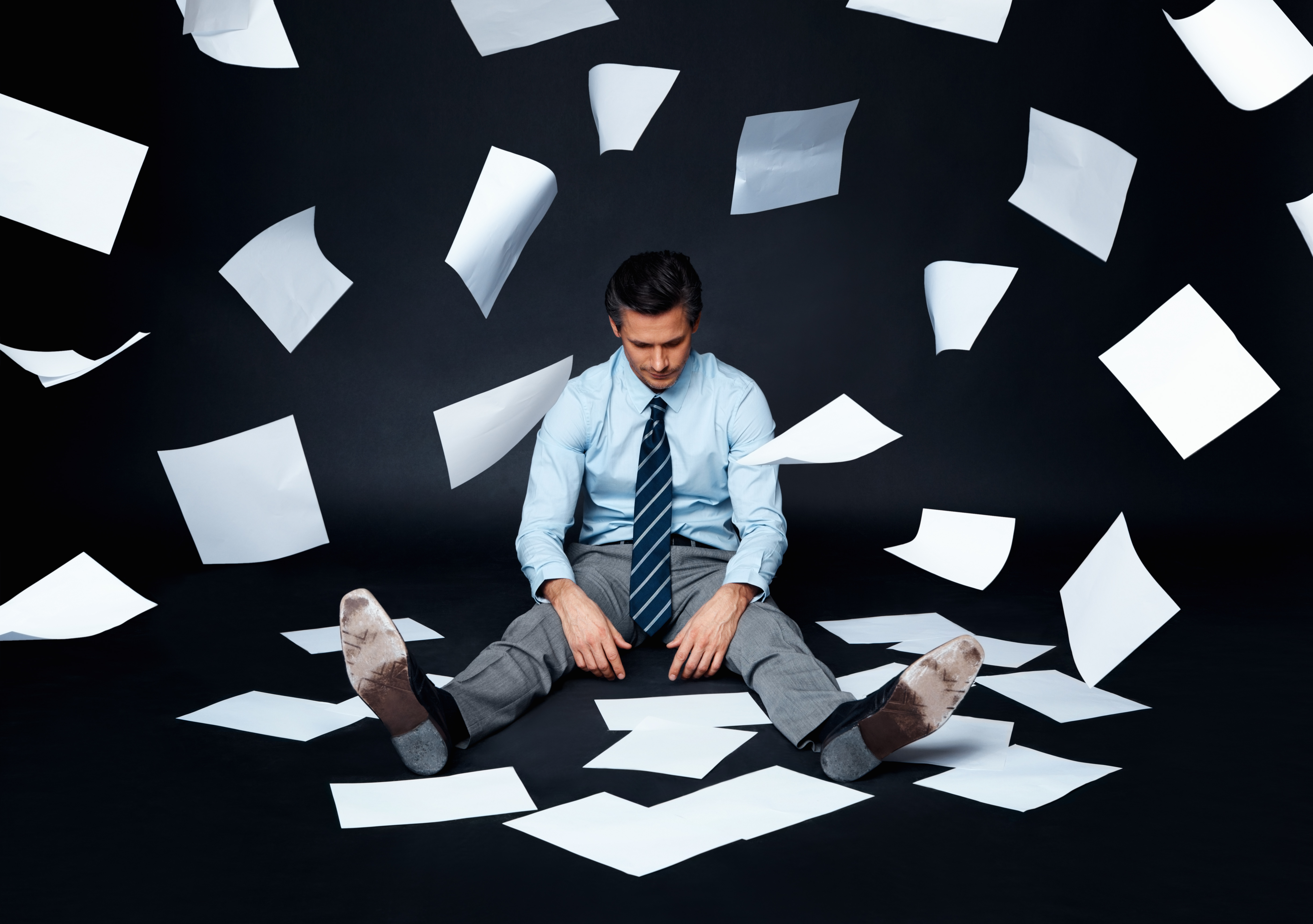 Stressed business man sitting on floor with papers falling around him