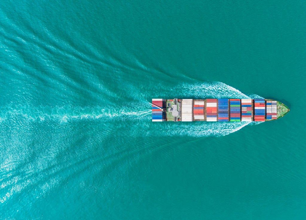Aerial top view container ship on the green sea full load container for logistics, import export, shipping or transportation.