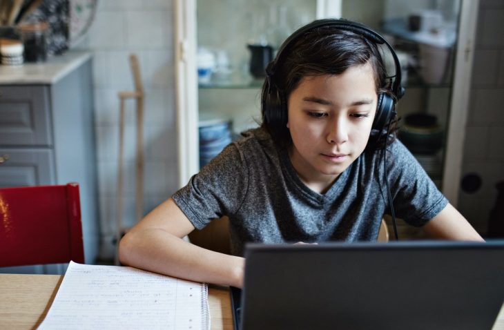 Boy wearing headphones while using laptop during homework at home