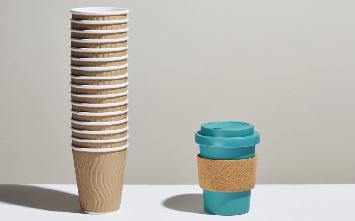 A stack of disposable coffee cups next to a reusable coffee cup