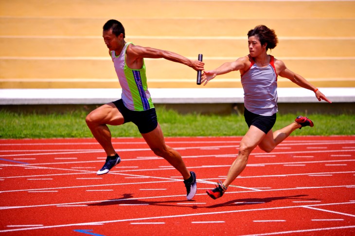 Two male athletes passing relay baton