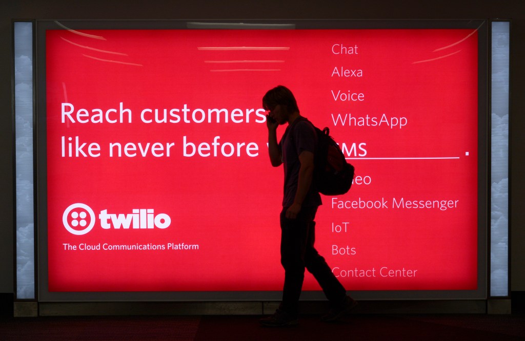 A passenger waiting to board his plane walks in front of a sign advertising Twilio at San Francisco International Airport.