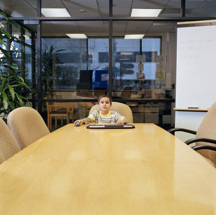 Boy (4-6) sitting at head of table in conference room, portrait