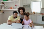 Two African American Parents Helping Their Daughter With Homework while using Laptop in the Kitchen at Home