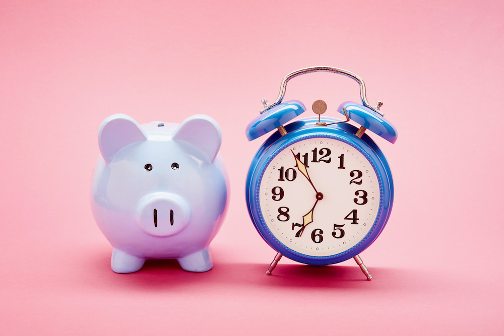 Retro alarm clock and blue piggy bank on pink background