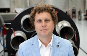 Rocket Lab CEO Peter Beck in a light blue suit in front of a rocket.