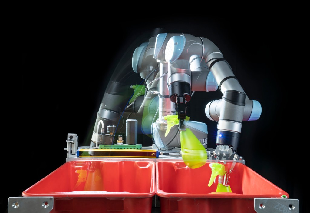 A robotic arm moves an item between two tubs.