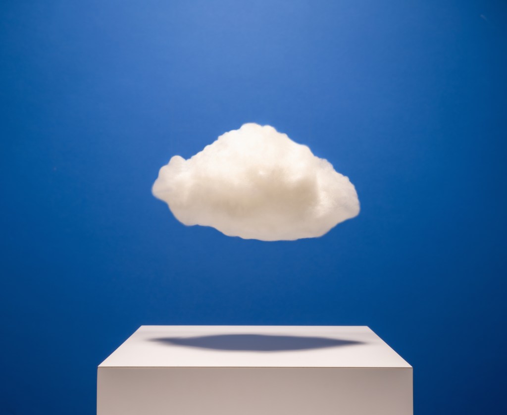 White cloud hovering over white surface with drop shadow on blue background, studio shot