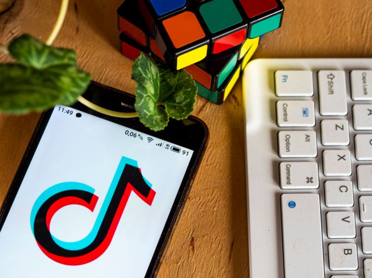 In this photo illustration a TikTok logo displayed on a smartphone next to a rubik's cube, a computer keyboard and a leaf.