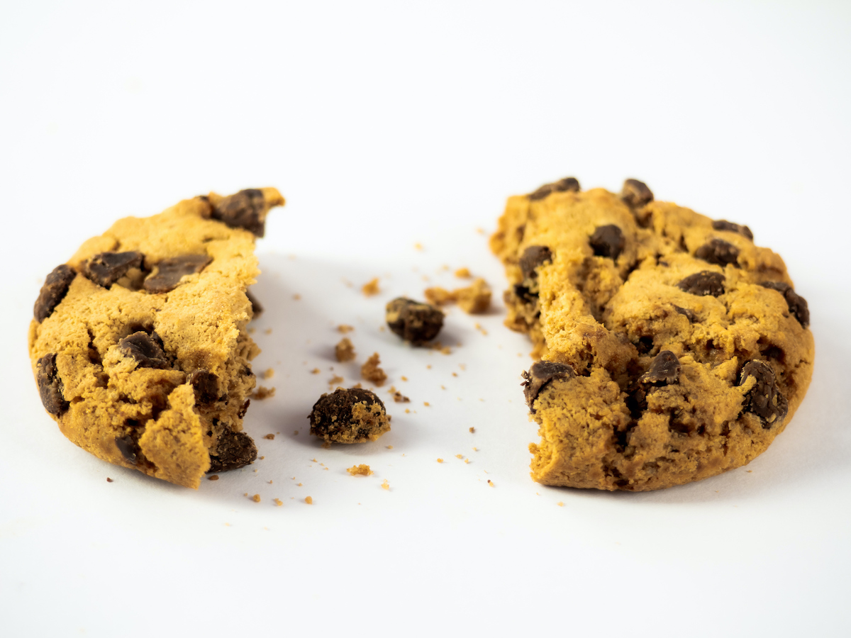 A homemade chocolate cookie with a bite and crumbs on a white background