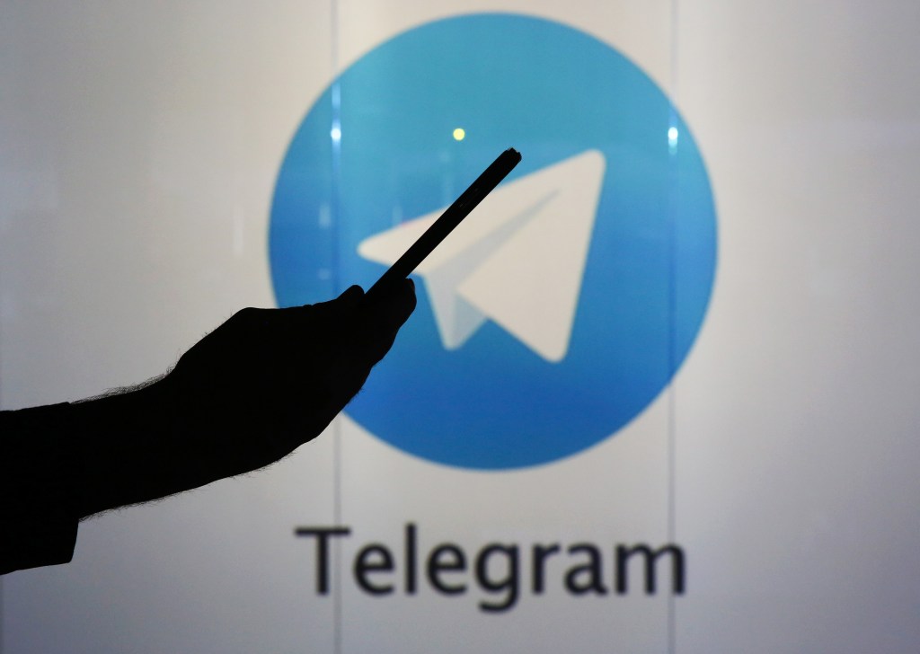 Logo de télégramme derrière la silhouette d'une personne vérifiant un appareil mobile