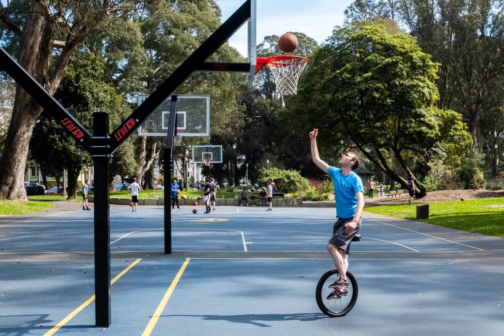 unicycle rider attempts to make a basketball layup in golden gate park