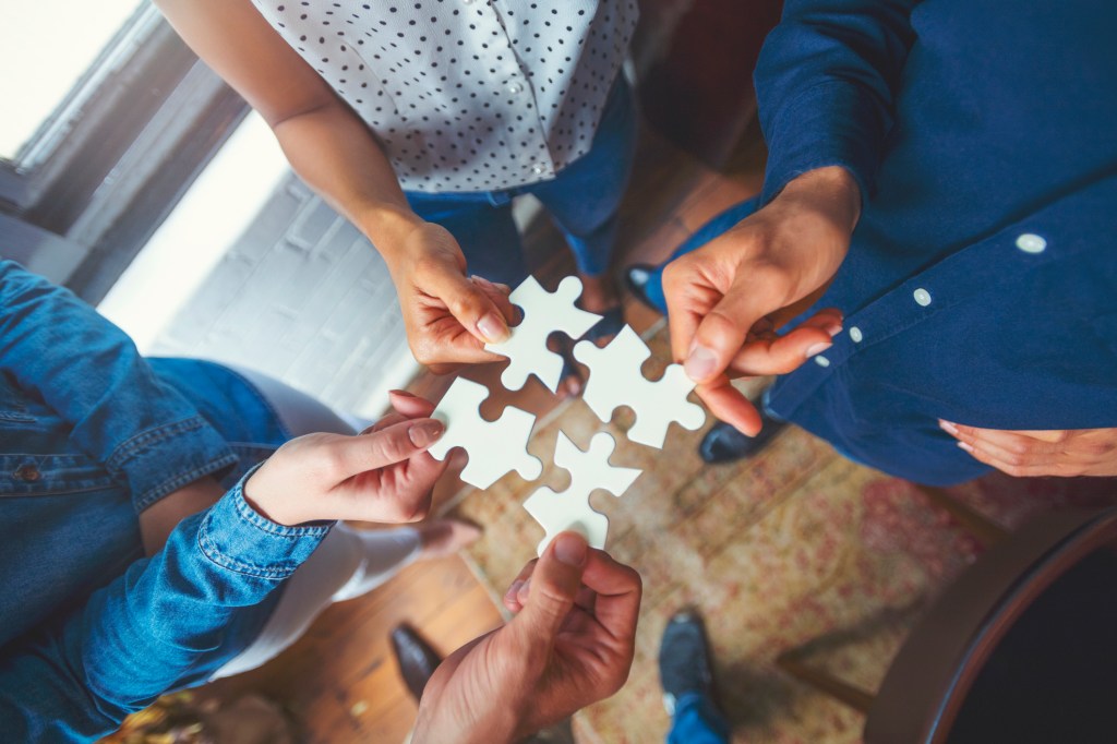 Group of business people holding a jigsaw puzzle pieces. Jigsaw pieces fit into each other. Business solution integration concept. Multi ethnic group. Close up of hands. high angle view directly above