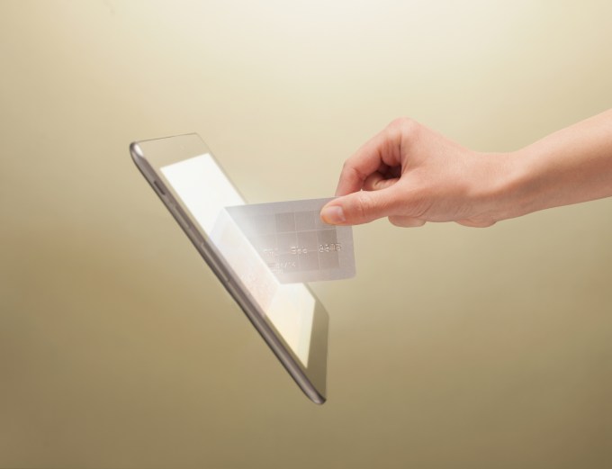 Female hand holding credit card partially in screen of a digital tablet