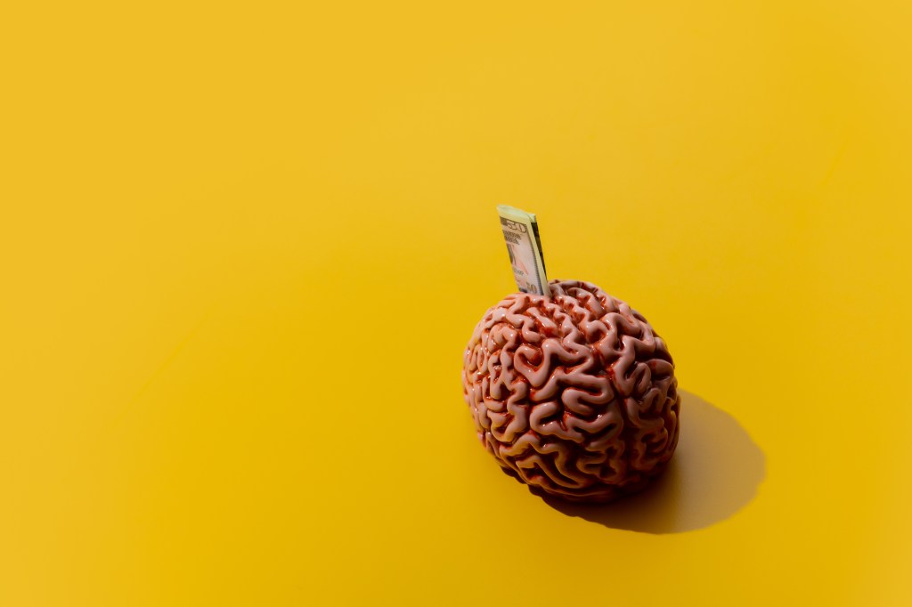 Image of money sticking out of a brain against a yellow background