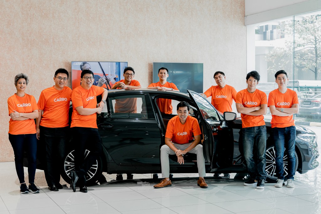 A team photo of Carro employees standing around a black sedan