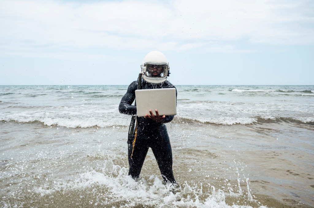 Astronaut using laptop on the beach