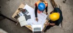 Image of two construction workers examining blueprints next to a laptop to represent tech on construction sites.