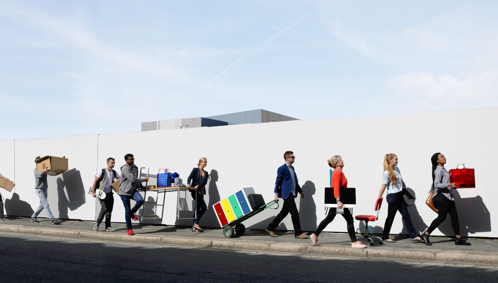 Office workers walking in a line on the street with office equipment