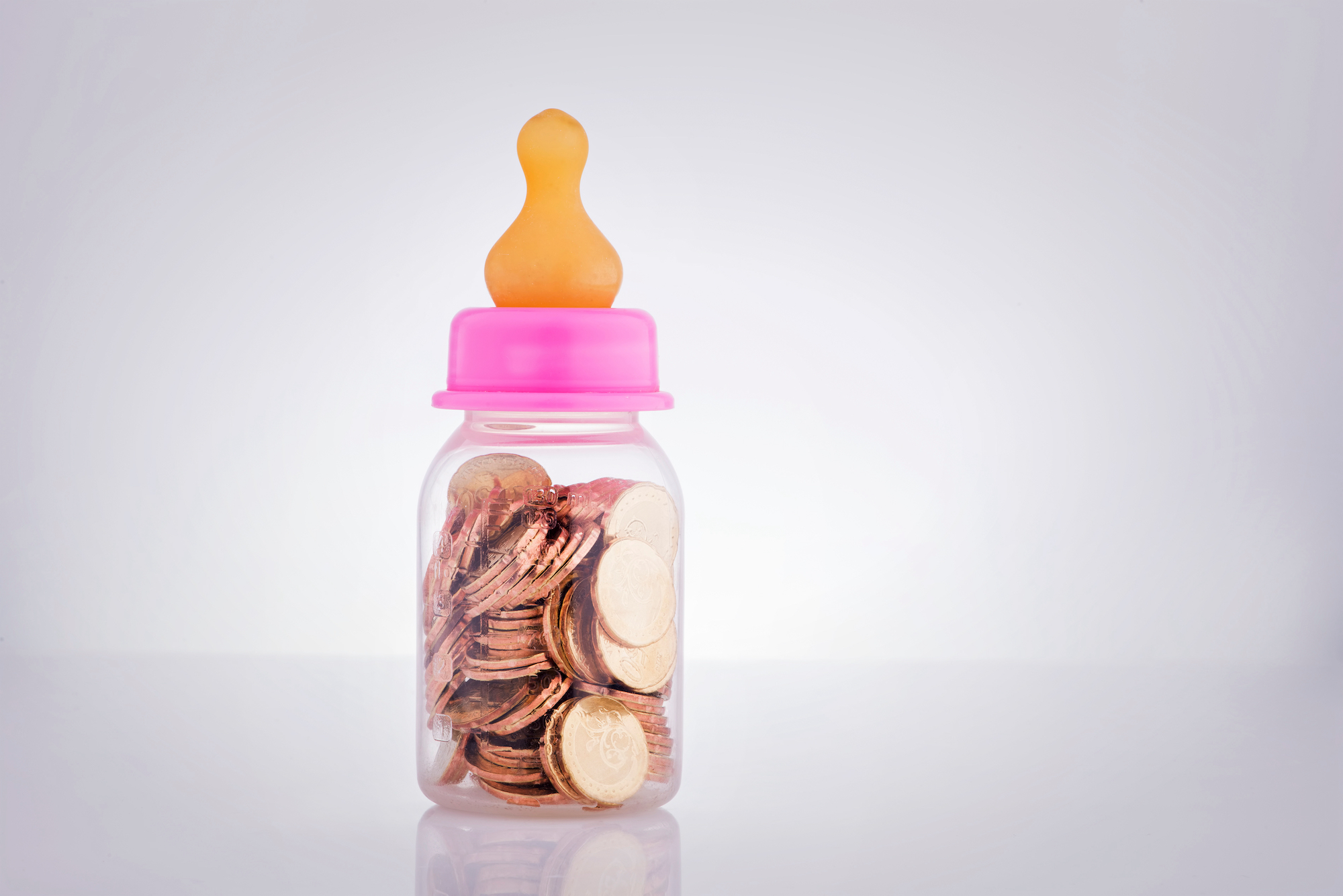 A baby bottle filled with coins on a white background