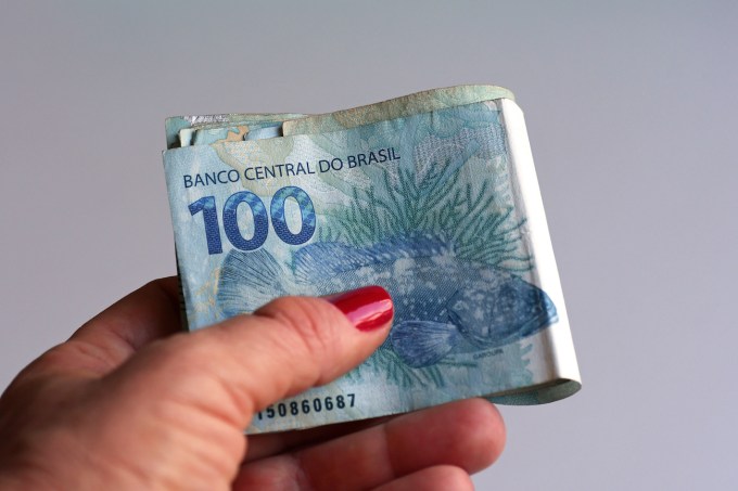 Mão feminina segurando dinheiro brasileiro (real / arroz)
