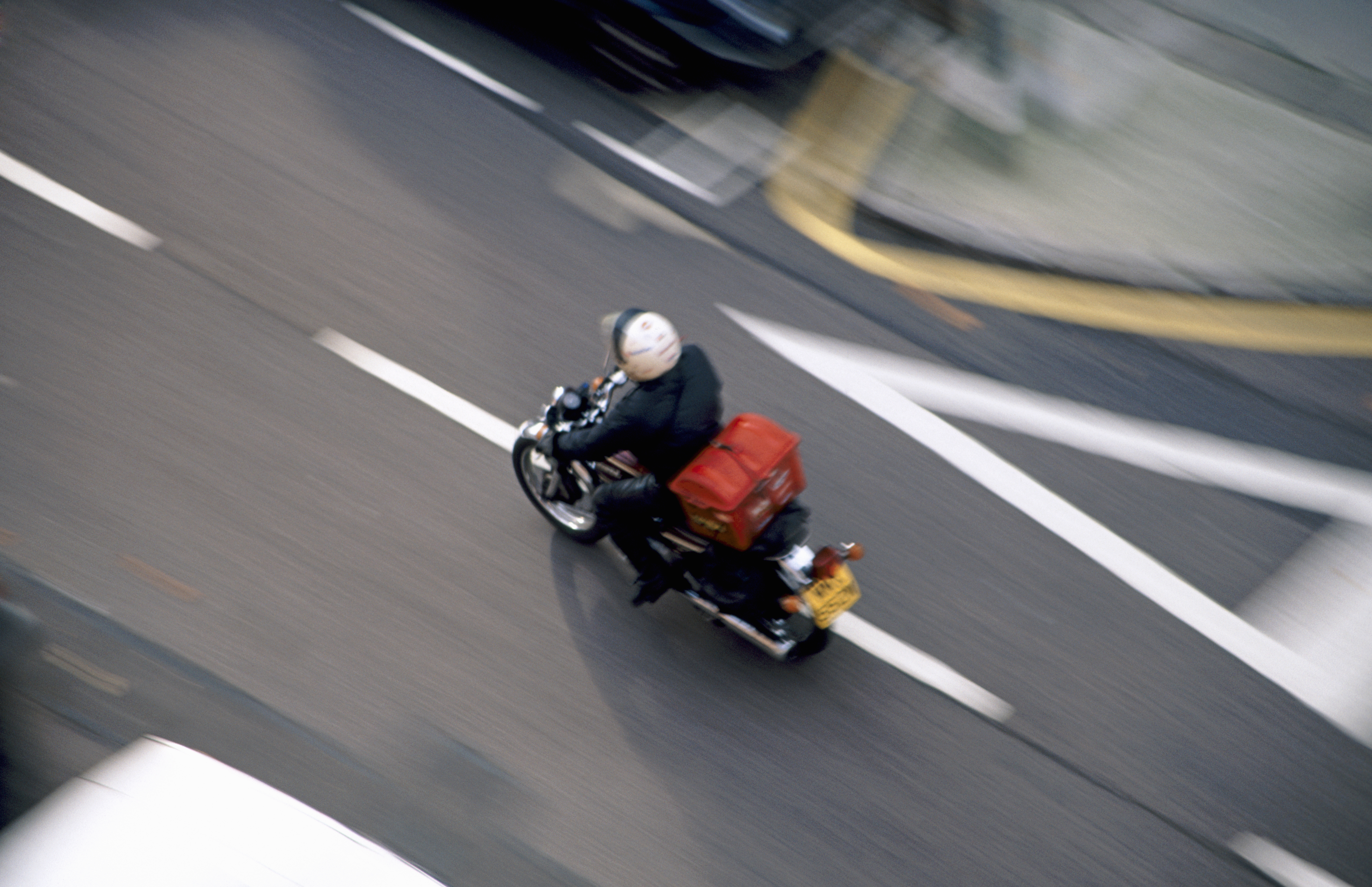 تصویری از پیک موتورسیکلت که با سرعت از خیابان عبور می کند.