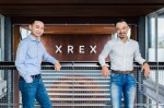 Blockchain startup co-founders Winston Hsiao and Wayne Huang in front of the company's logo