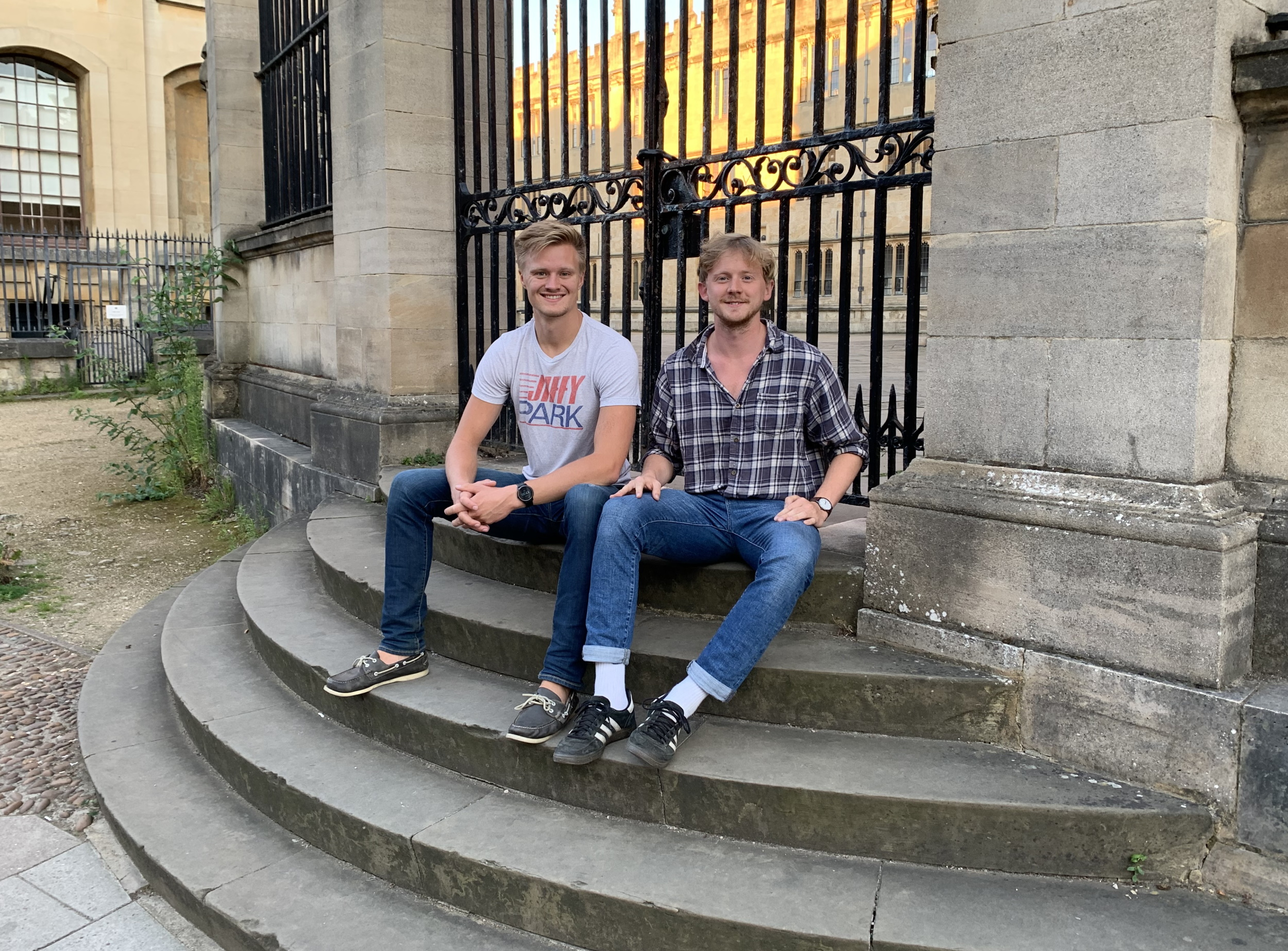 Heimdal founders Marcus Lima (left) and Erik Millar sitting by a metal gate on stone steps..