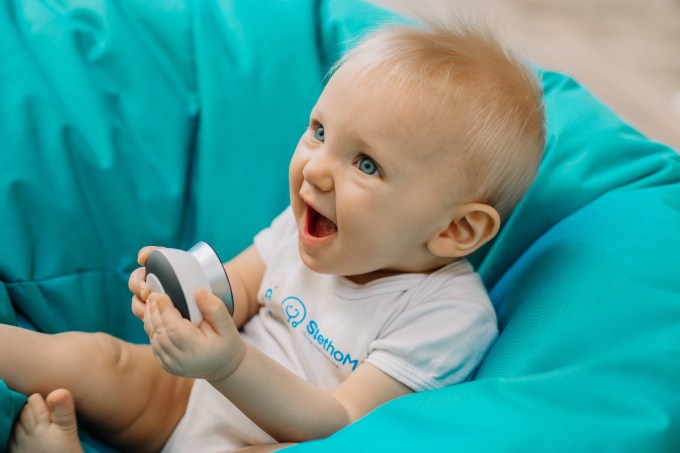 A baby holding a StethoMe device which can listen to kids' lungs so doctors can hear them from afar.