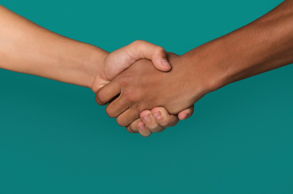 Handshake of Black and white teens shaking hands, against blue background, closeup