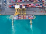 Aerial view of tugboats pushing a container cargo ship into a loading dock, taken in Thailand