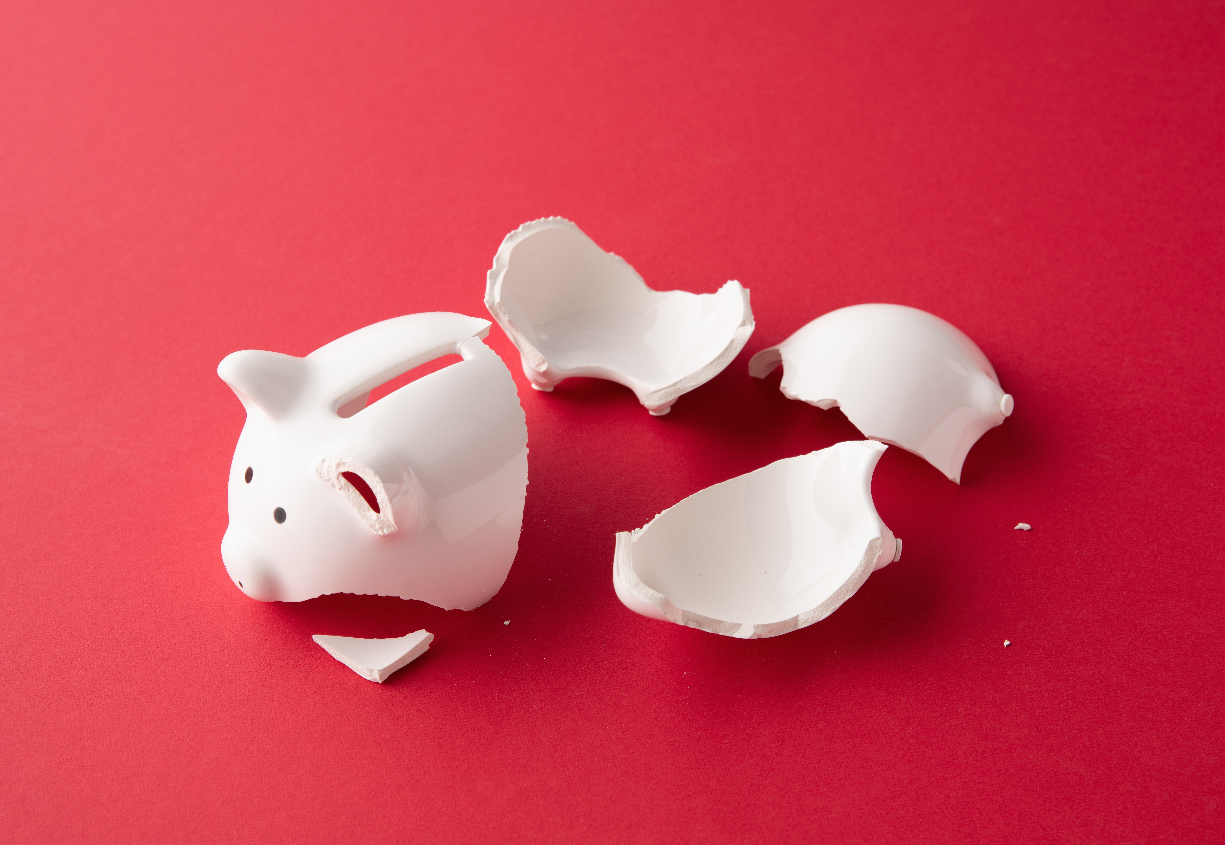 Image of a broken white piggy bank on a red background.