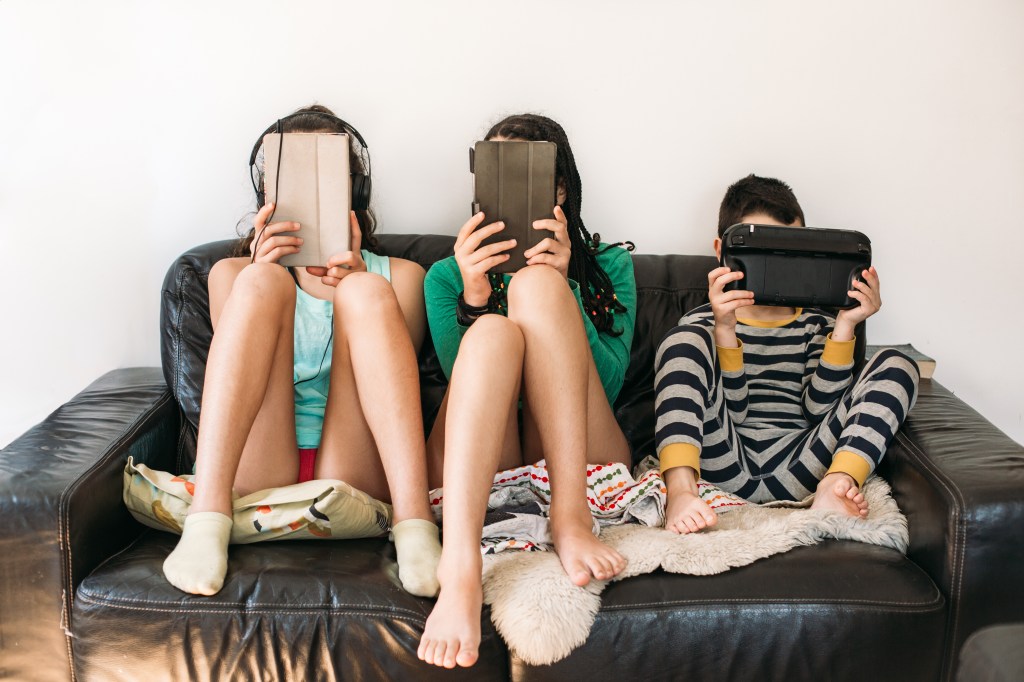 Three kids holding tablets sit on a couch