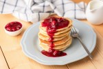 Pancakes with cherry sauce on wooden table. Tasty breakfast