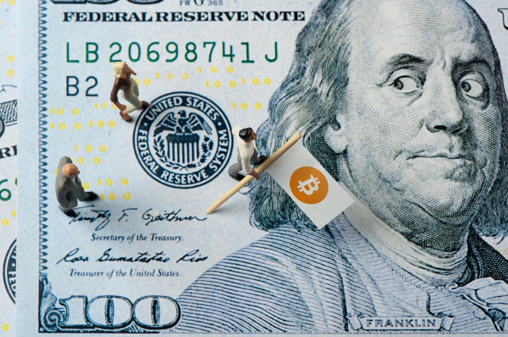 Image of figures with bitcoin flag walking on hundred-dollar bill.