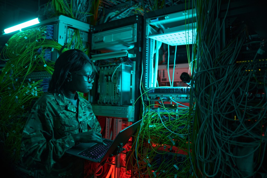 Side view portrait of young African-American woman wearing military uniform inspecting server while working in server room