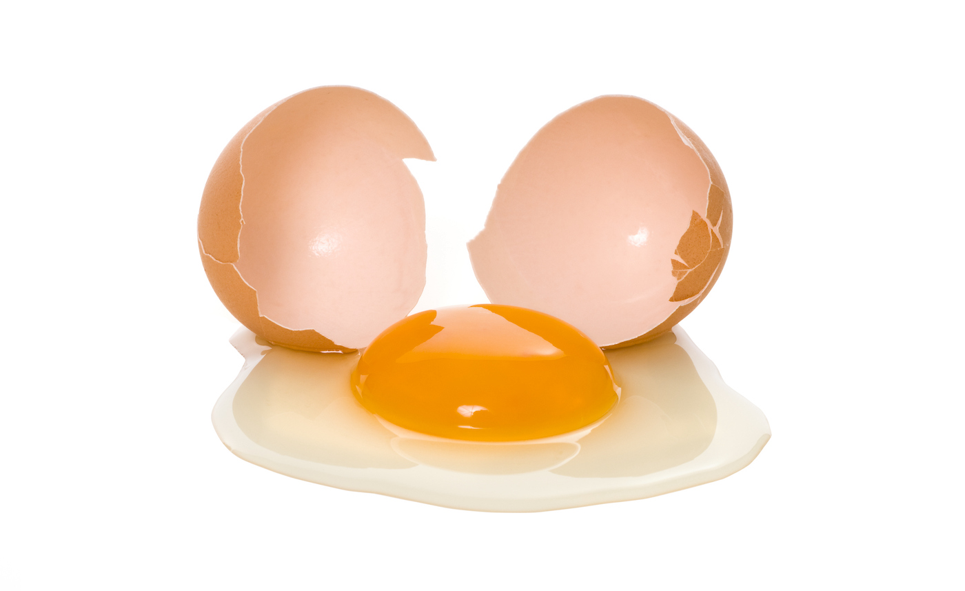 Beyaz arka planda kahverengi kabuğu olan kırık bir yumurtanın yakın plan fotoğrafı.