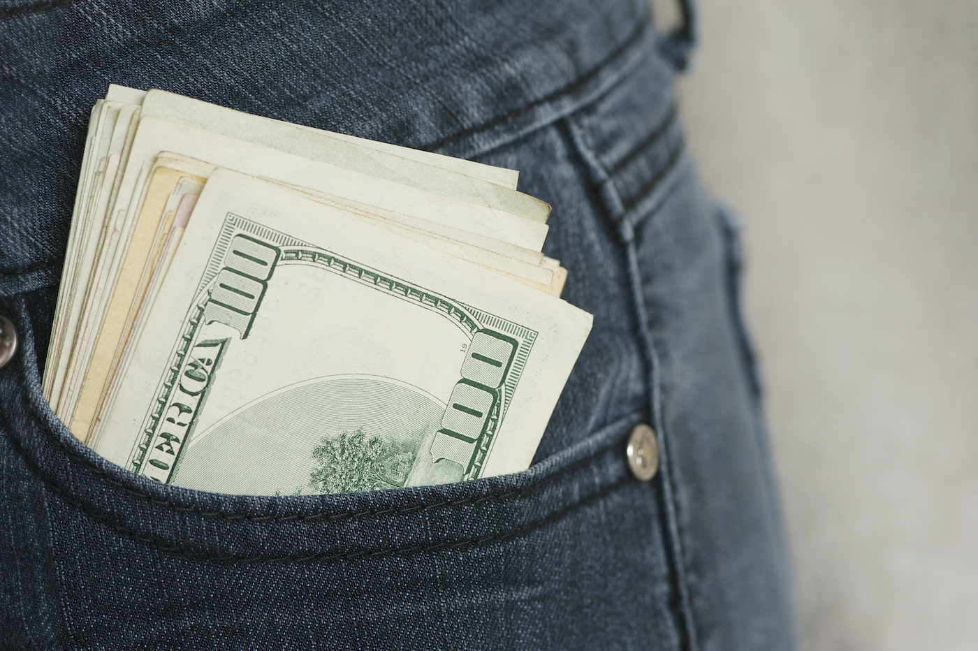 Cash bills in a sizable stack protrude from a jeans front pocket