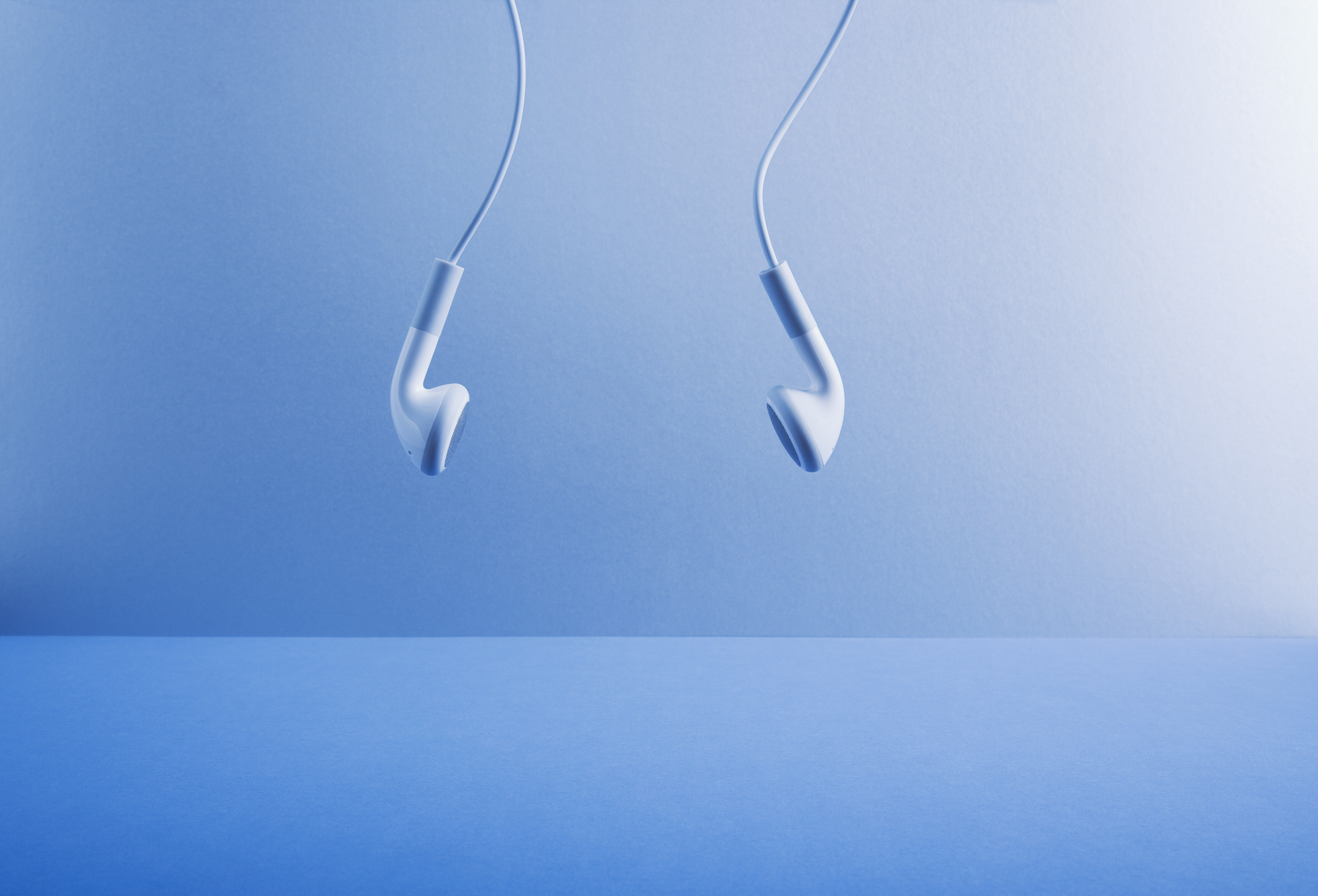 Image of white headphones hanging against a blue background.